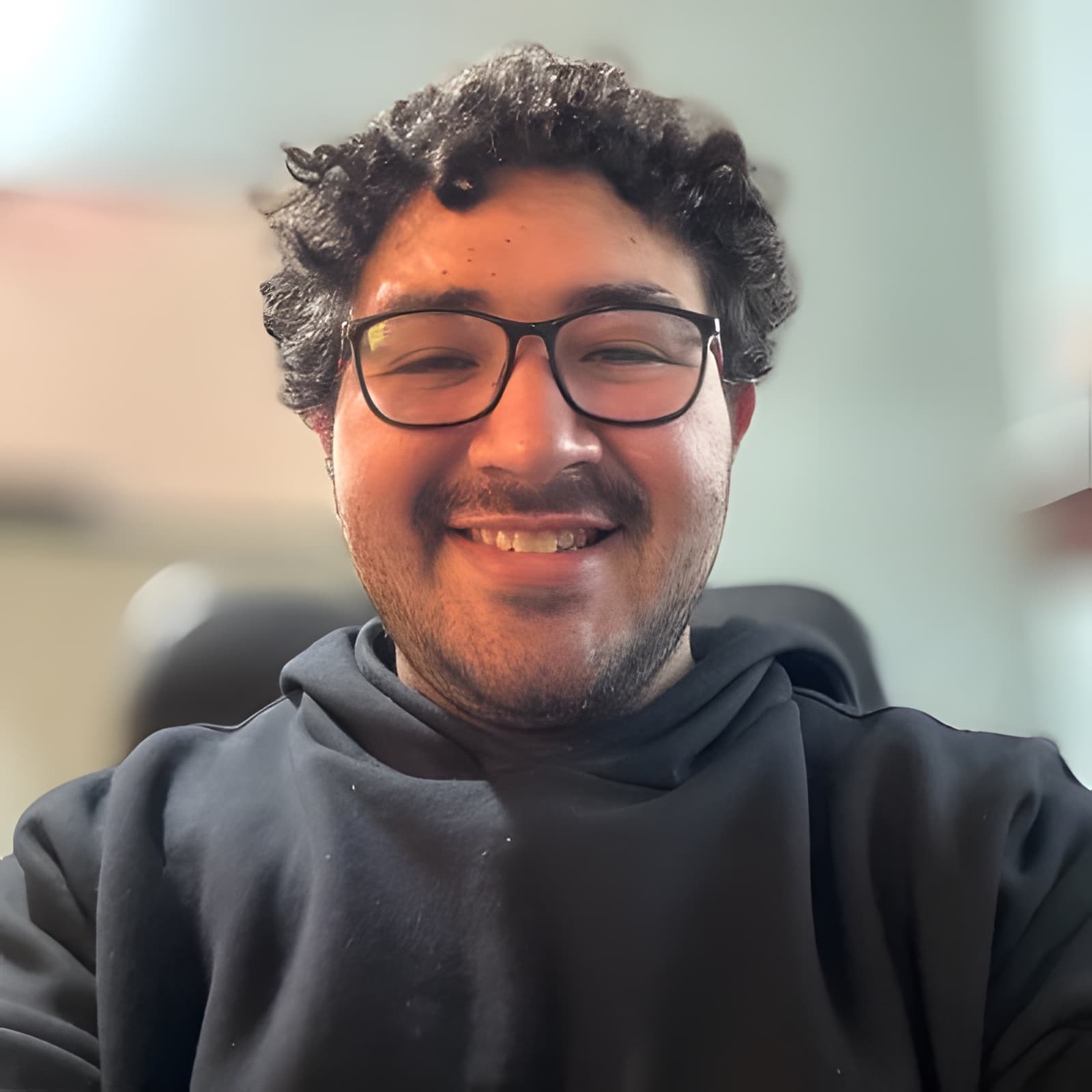 Portrait of Alexis smiling, wearing glasses and a black hoodie